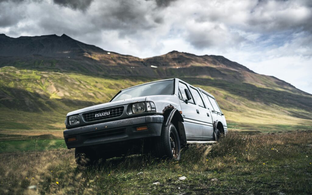 An abandoned Isuzu vehicle rusting in the serene Icelandic mountains under a cloudy sky.