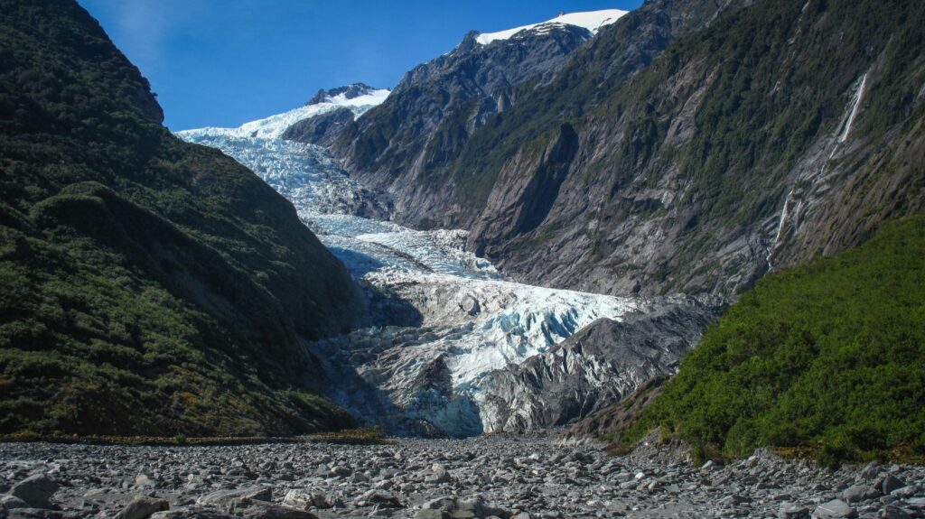 Captivating view of a glacier nestled between rugged mountain valleys under a clear blue sky.