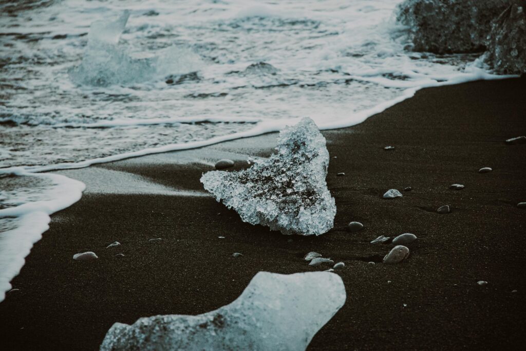 Glistening icebergs rest on the volcanic black sand shore in Iceland, creating a surreal seascape.