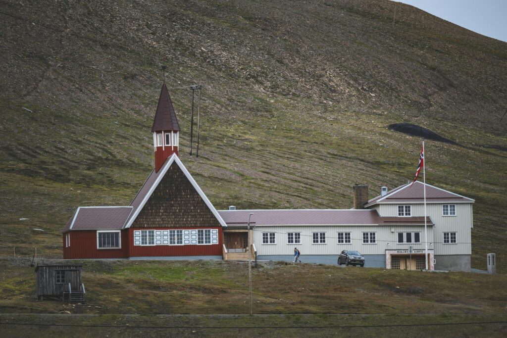 A scenic view of a red church in Svalbard, Norway, set against a mountainous landscape.