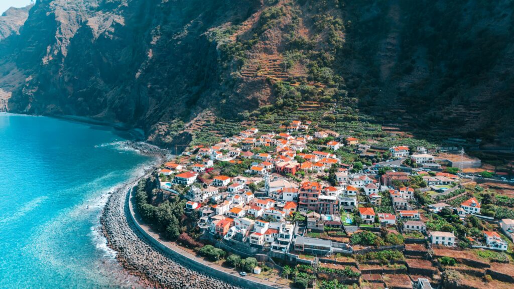 Stunning aerial view of a coastal town in Madeira, Portugal, with lush cliffs and turquoise sea.