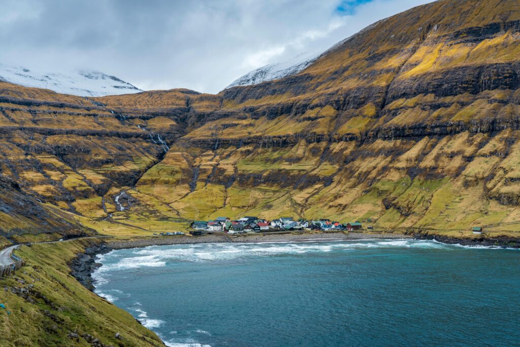 Coastal village in Faroe Islands surrounded by cliffs and ocean under a cloudy sky.