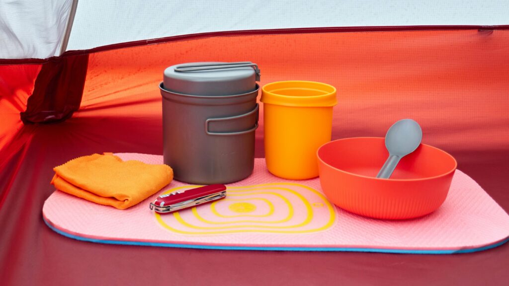 Colorful camping cookware and utensils arranged neatly inside a tent.