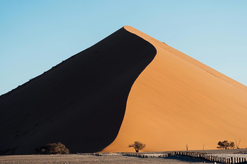 Capture of a striking sand dune in the Namib Desert with dramatic shadows and clear blue sky.