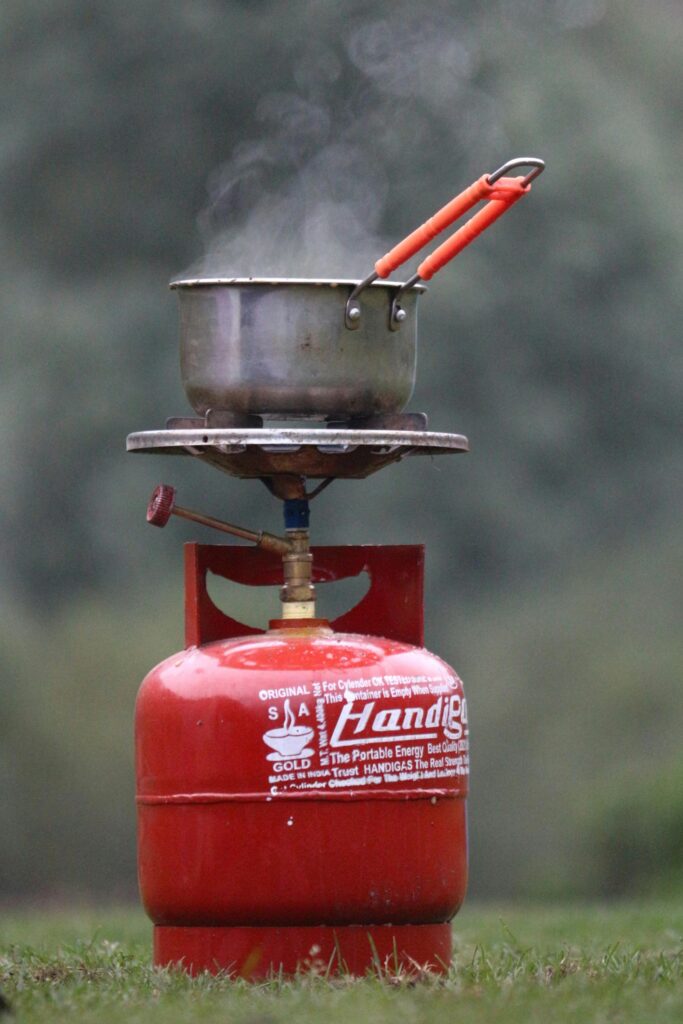 Steam rises from a pot on a portable red gas cylinder stove outdoors, suggesting camping ambiance.