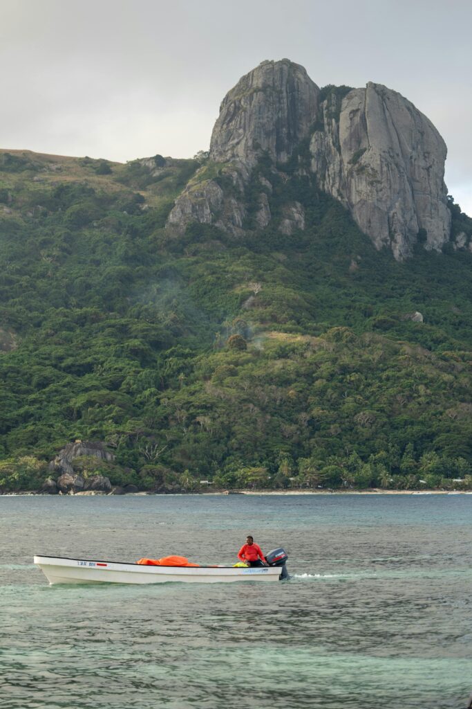 Explore the stunning coastal landscapes of Fiji with a lone boat on calm waters and a majestic mountain backdrop.
