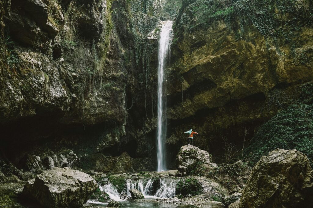 A breathtaking waterfall cascading in a lush New Zealand canyon with a person exploring nearby.