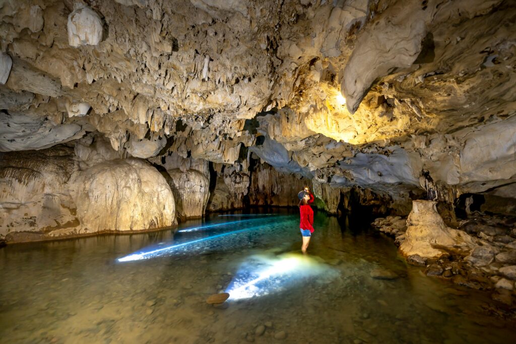 A person explores a fascinating limestone cave, illuminated by natural light.