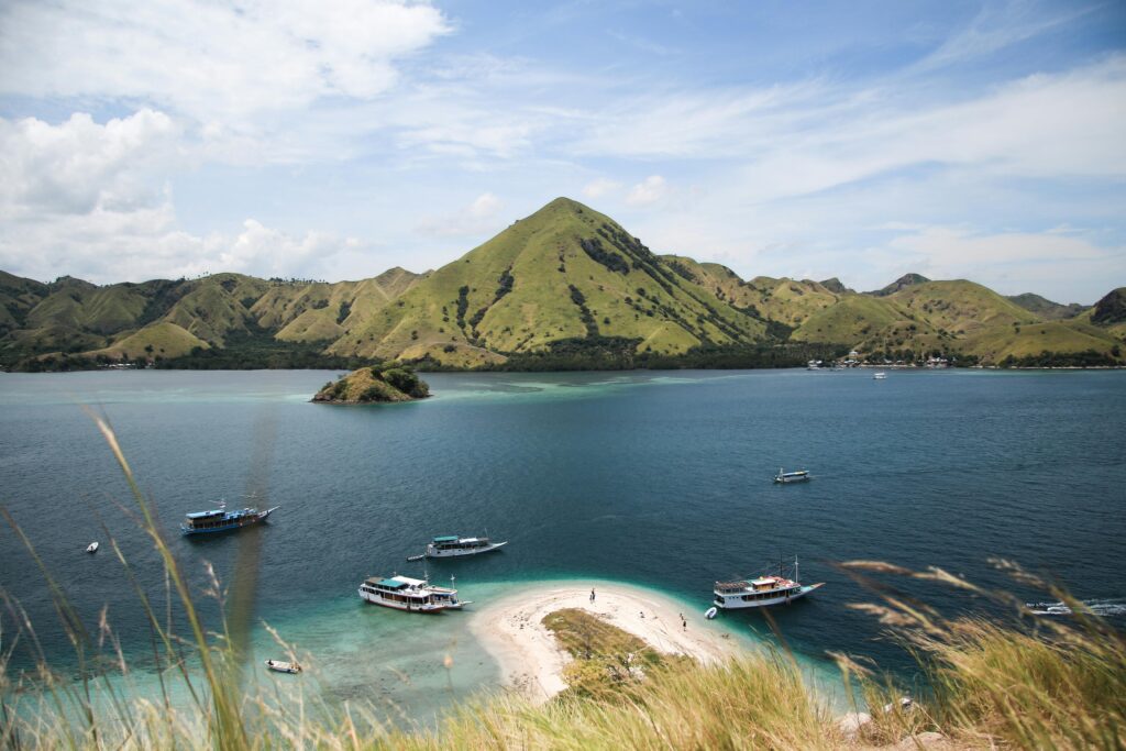 Explore the breathtaking beauty of Komodo Island with boats and lush mountains under a clear sky.