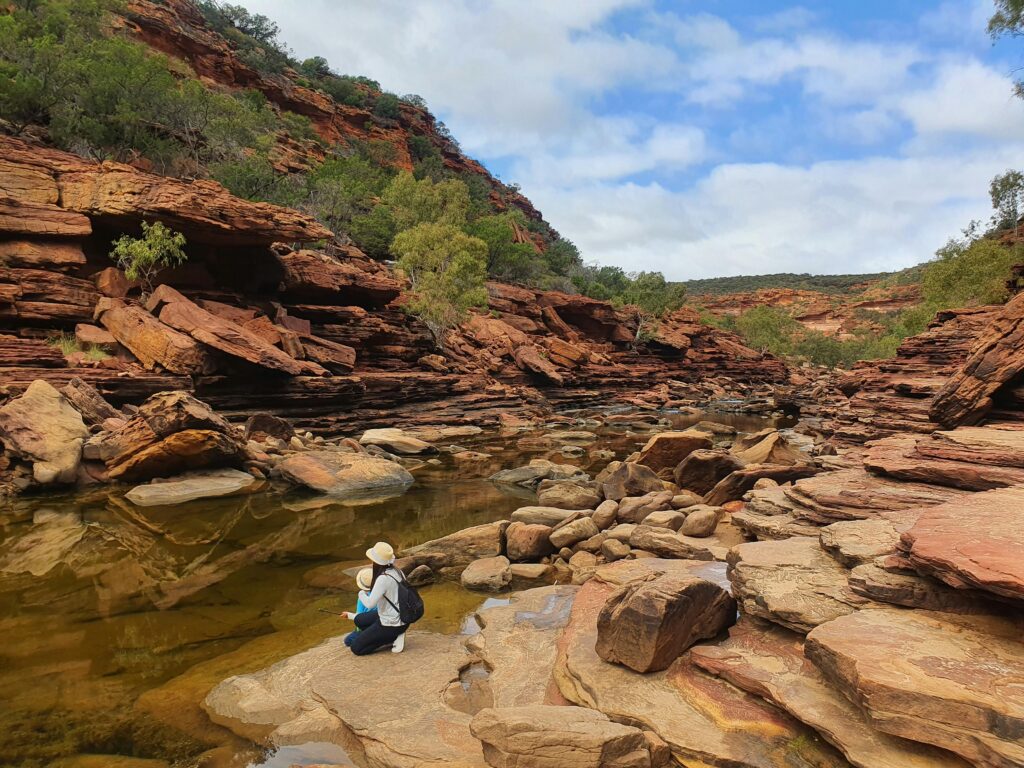 A woman enjoys the serene beauty of Z Bend Gorge, Kalbarri National Park, with stunning rock formations and reflections.