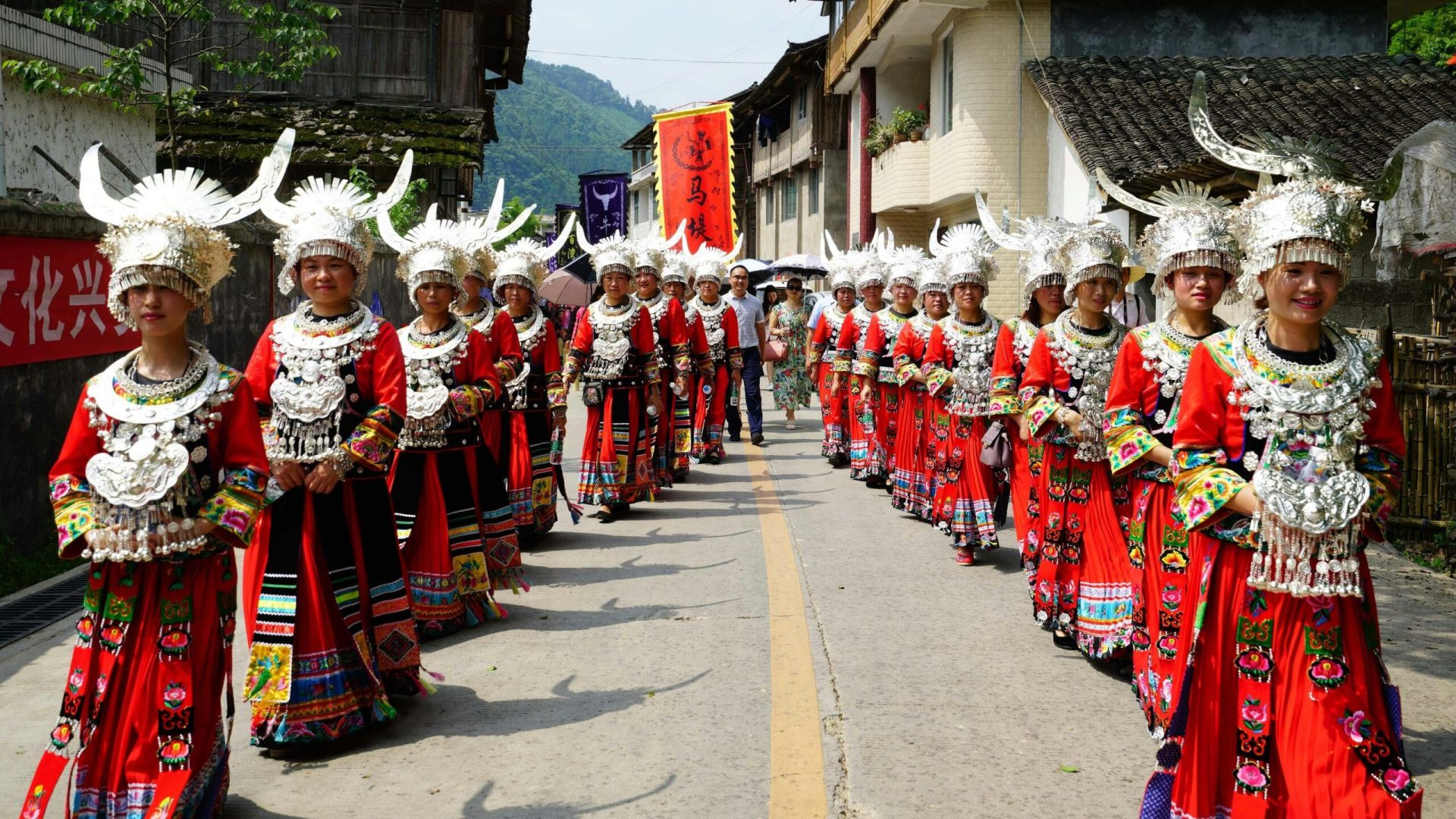 Colorful Miao women in traditional attire during a street parade in rural China.