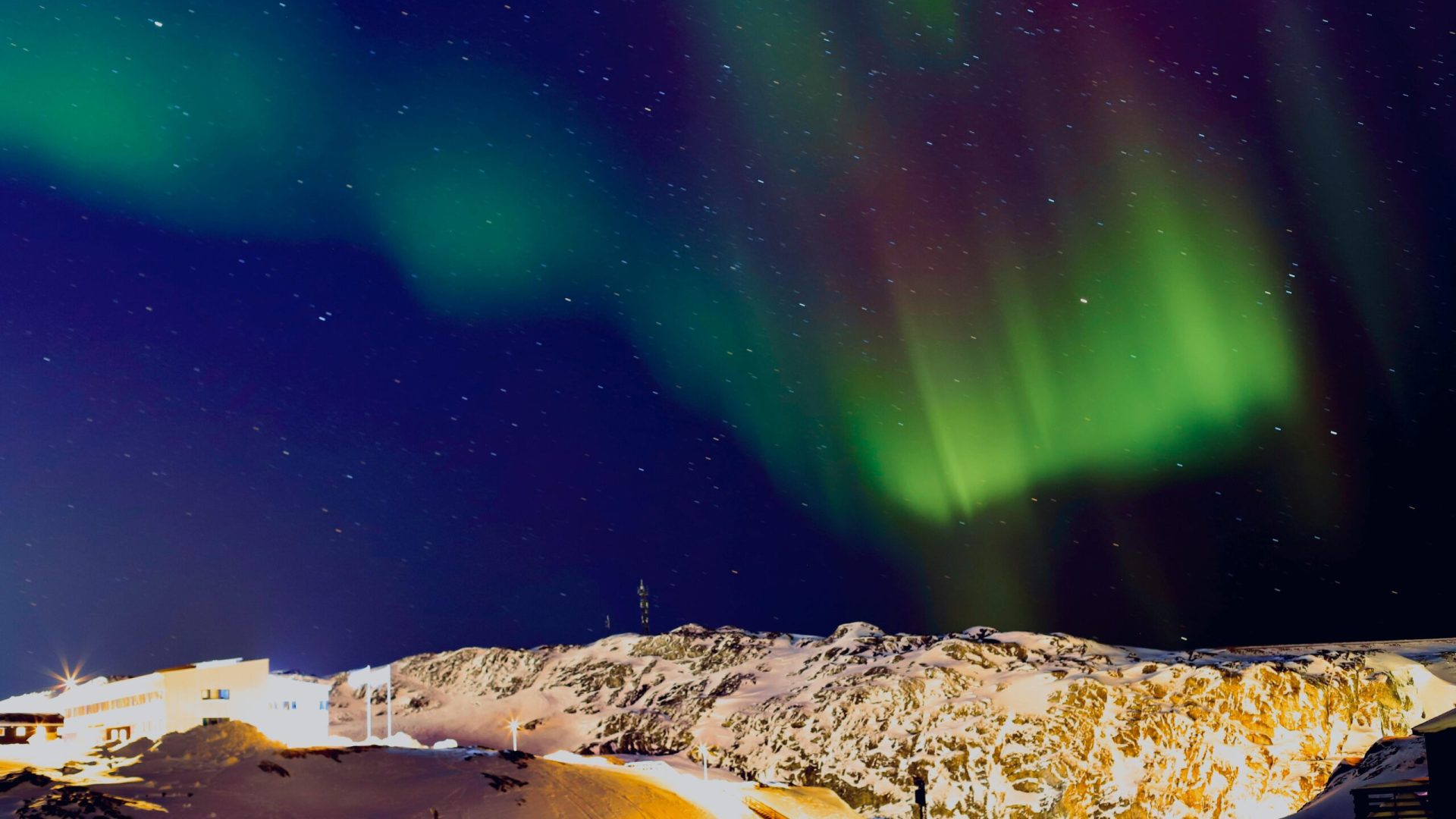 Stunning northern lights display over snowy mountains and starry night sky.