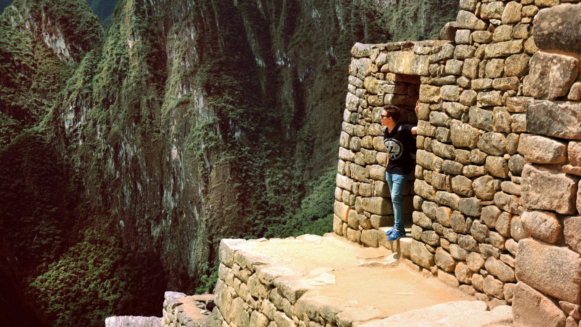 Man at Machu Picchu doorway overlooking lush mountains, capturing Inca architectural marvels.