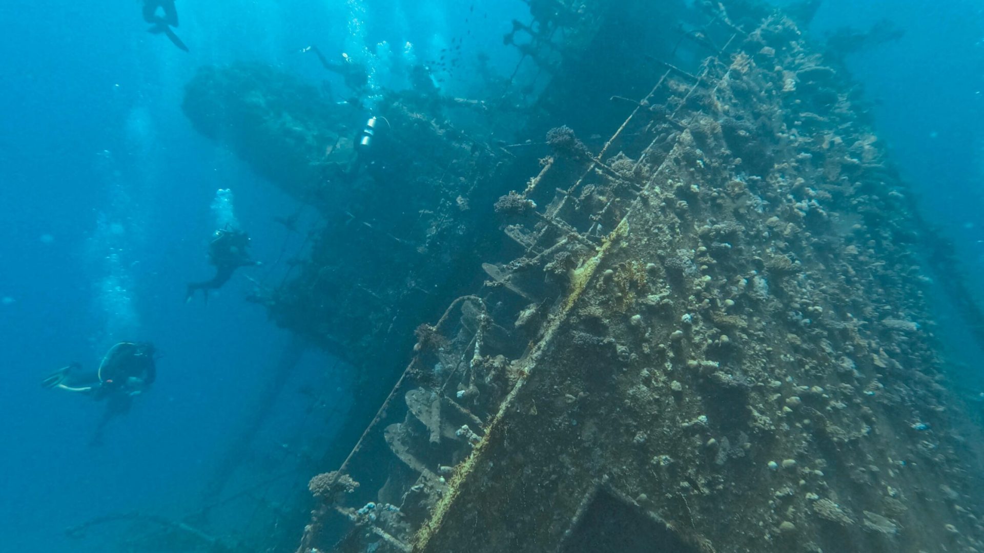 Explore a sunken shipwreck with scuba divers navigating through clear blue waters.