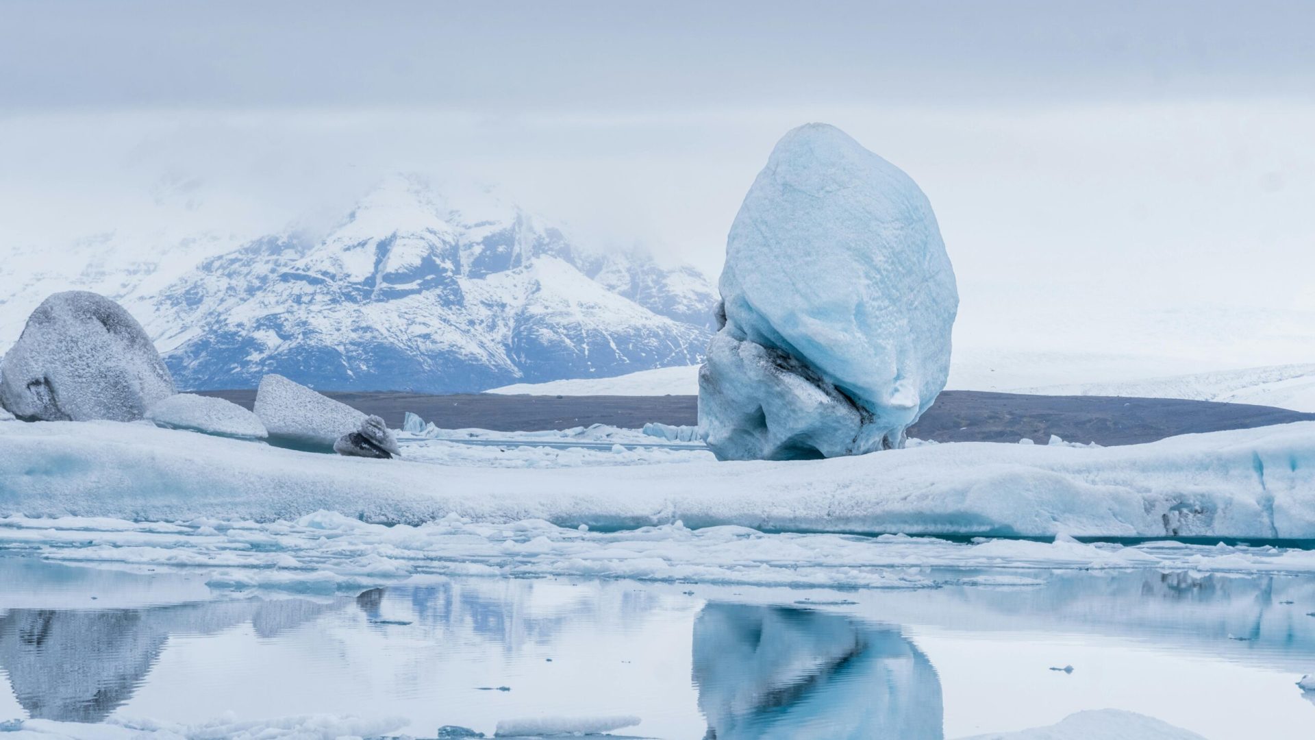 A stunning view of a glacier and snowy mountain reflected in a pristine icy lagoon under a winter sky.
