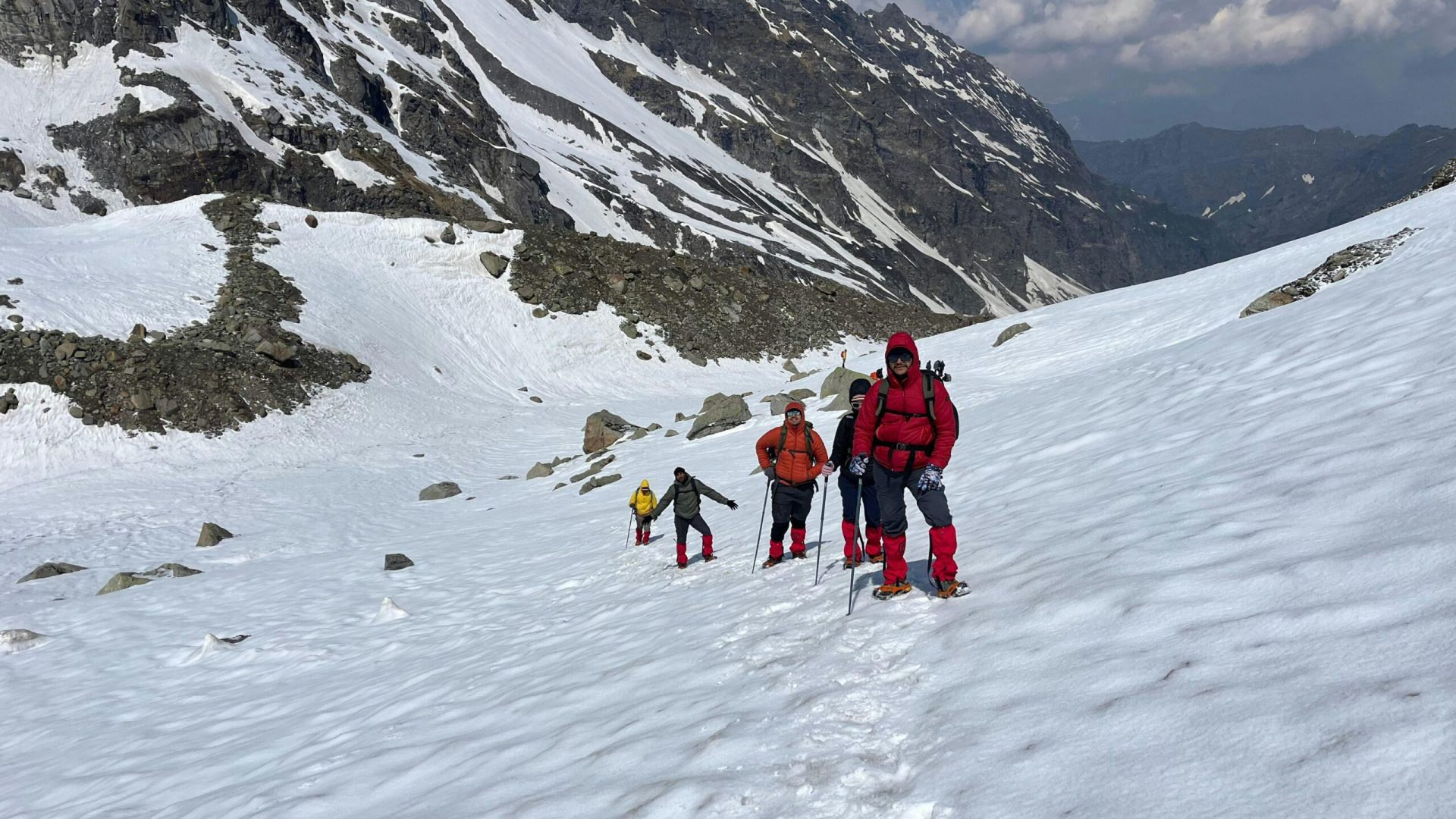 Adventurers trekking through snow in Hampta Pass, Himalayas. Experience majestic alpine scenery.