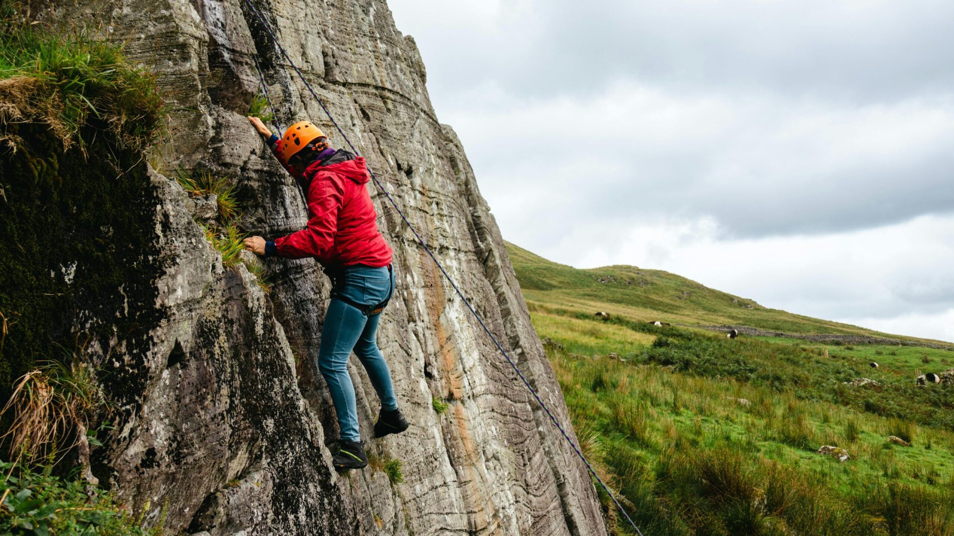 A person rock climbing on a rugged cliff in the English countryside, showcasing adventure and physical challenge.