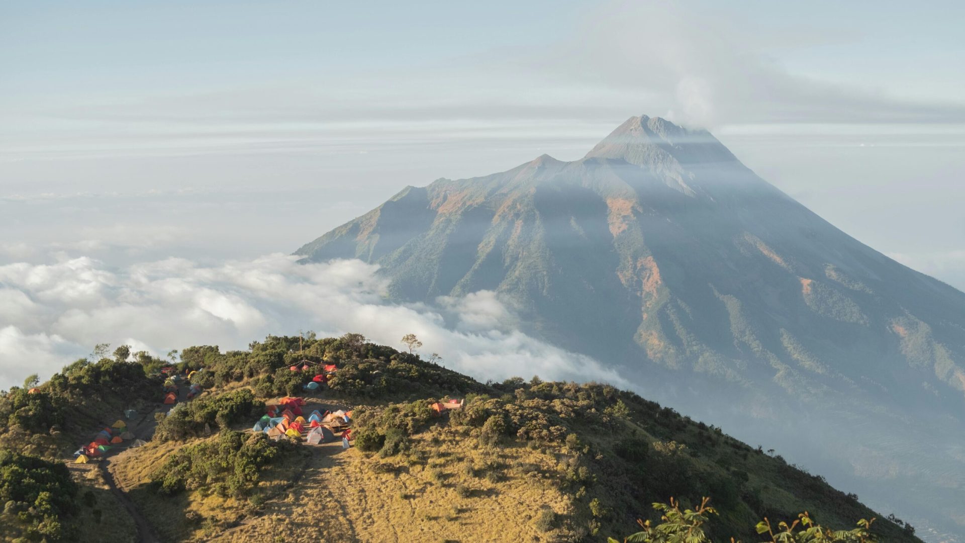 View of Mount Merapi with campsite amidst sea of clouds at sunrise.