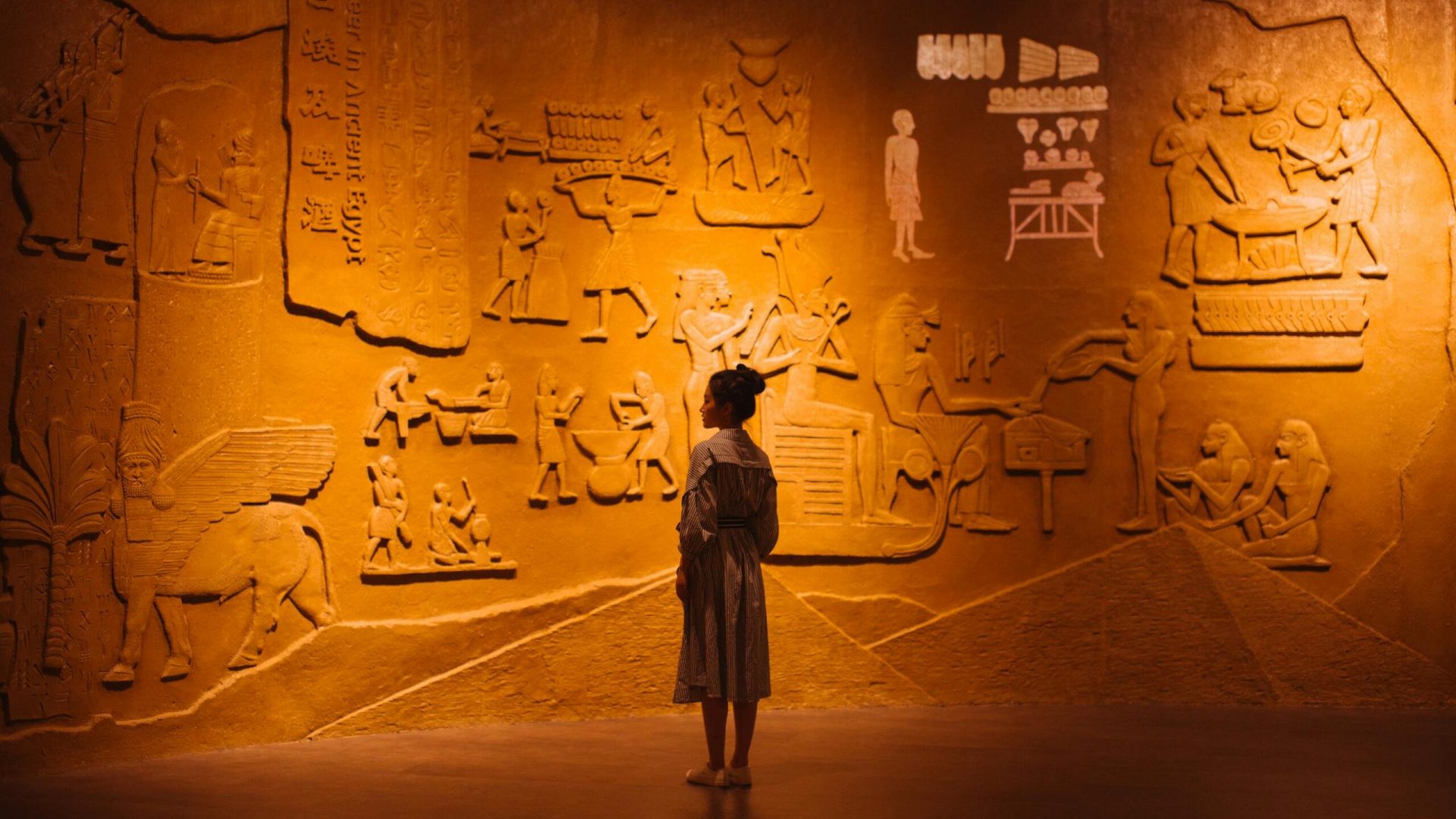 Back view of anonymous female traveler standing near ancient wall with Egyptian engraving