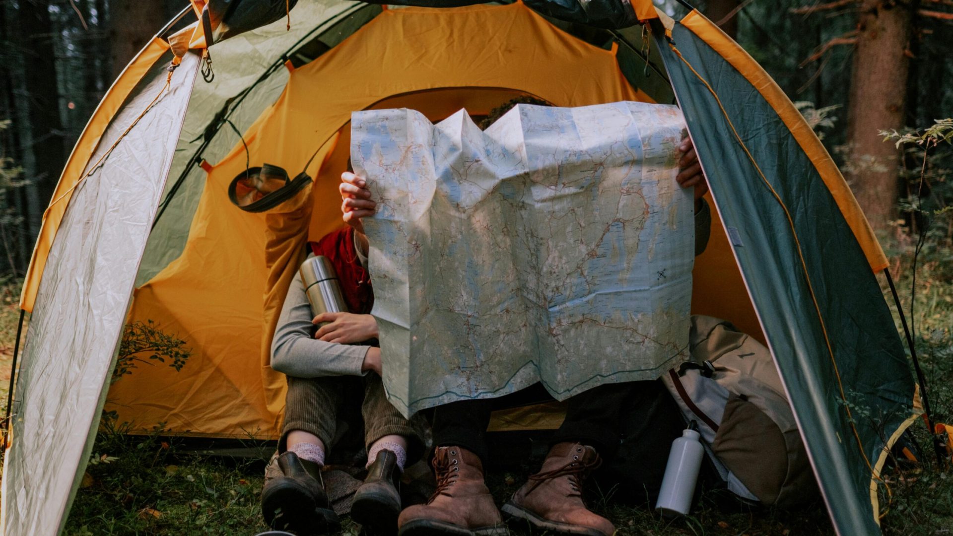 Two people enjoy a camping trip, examining a map inside a tent surrounded by nature.