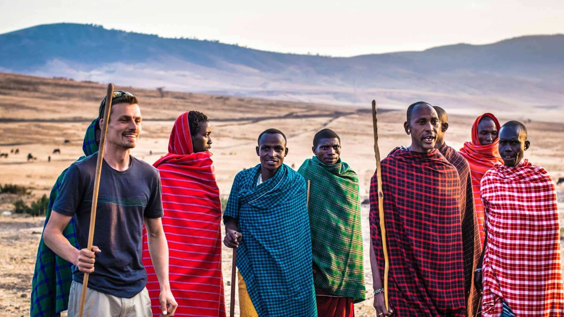 A traveler joins Masai tribe members on a sunny day in an open African landscape.